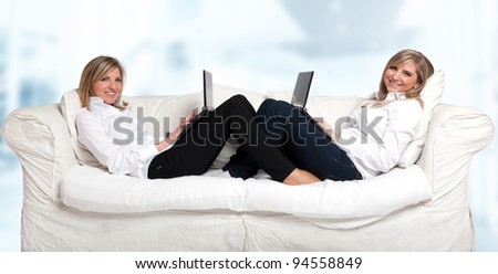 Two blonde young women sitting on the sofa with laptops in a symmetrical position