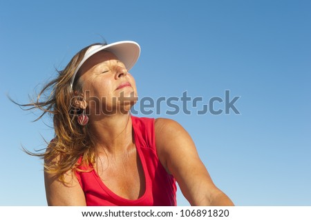Portrait of happy attractive looking middle aged woman joyful laughing, isolated with sunshine on face and blue sky as background and copy space.
