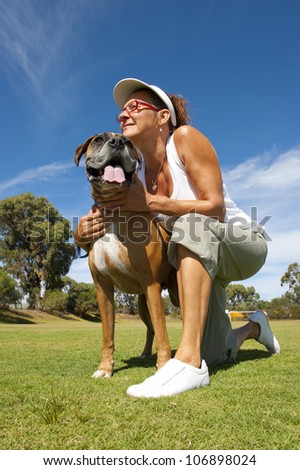 Woman owner with friend and big pet boxer bull dog in park, alert and training, exercising, isolated with blue sky as background and copy space.