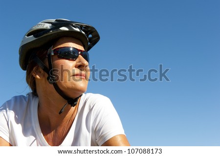 Portrait of healthy fit and sporty, confident and successful mature woman cycling on mountain bike, isolated with blue sky as background and copy space.