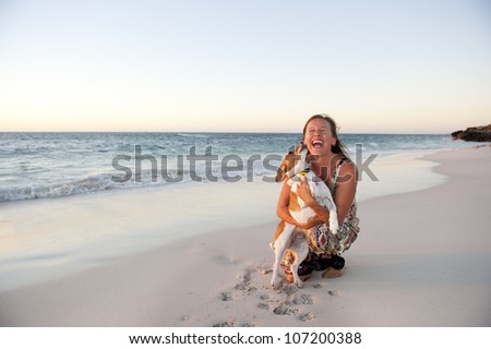 Happy looking mature woman is enjoying a sunset at the beach with her pet dog, with ocean and twilight sky as background and copy space.
