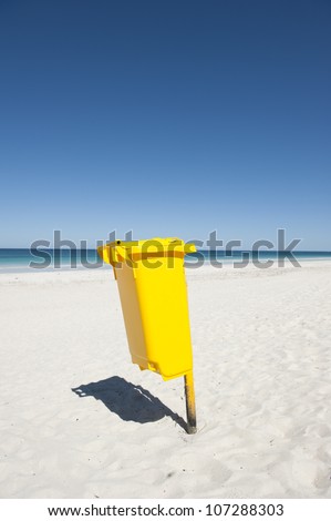 Bright yellow colored rubbish bin at remote tropical beach, to keep environment clean, isolated with ocean and blue sky as background and copy space.