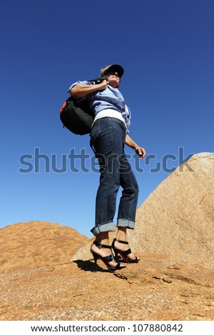 Mature woman in jeans and high heel shoes walking, traveling, hiking through Devils Marbles in Australian outback.
