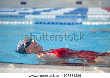 Mature woman in red bathers doing swim exercises, keeping healthy and fit in swimming pool.