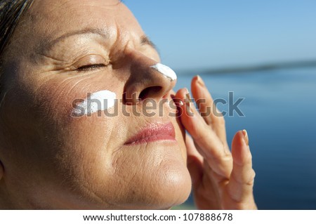 Portrait of attractive mature woman with suncream on her face to protect herself from skin cancer, isolated with blurred background and copy space.