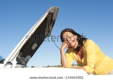 Stressed mature woman breakdown with car on remote road waiting for assistance, for help, isolated with blue sky as background and copy space.