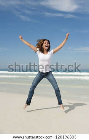 Happy cheerful young sexy woman jumping full of joy at beach with arms up, isolated with ocean and blue sky as background and copy space.