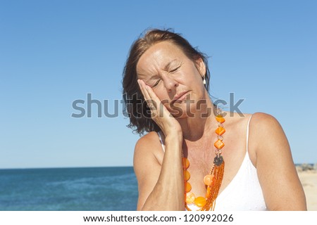 Portrait lonely mature woman having migraine or menopause symptoms, isolated with ocean and blue sky as background and copy space.