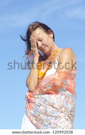 Portrait Beautiful mature woman having migraine or menopause symptoms, isolated outdoor with blue sky as background.