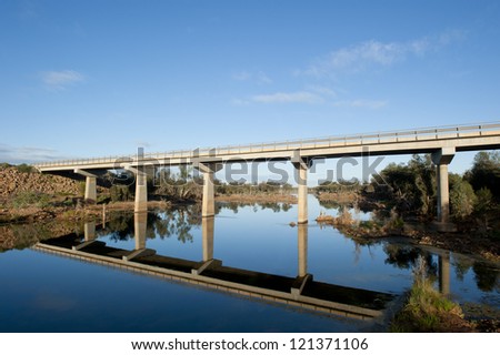 Highway bridge over Murchison River in Western Australia, with lush outback vegetation along the river bank and blue sky as background.