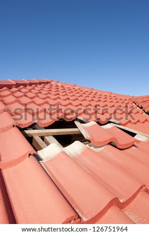 Damaged roof construction on house needs tiles or shingles repaired and replaced, red tiles and blue sky as background and copy space.