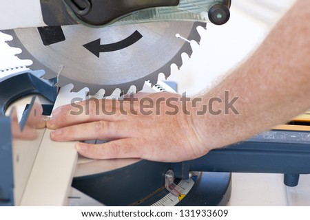 Closeup of sharp circular saw blade and hand of carpenter or worker, concept image safety and security at workplace.