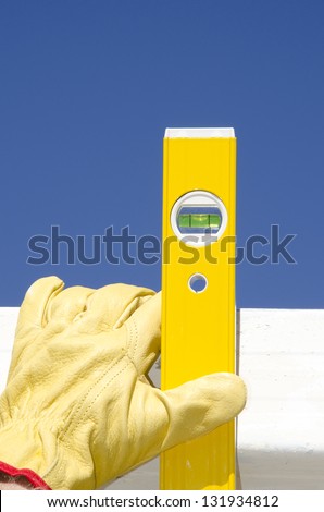 Hands of construction worker with gloves on spirit or water level tool outdoor, with blue sky as background and copy space.