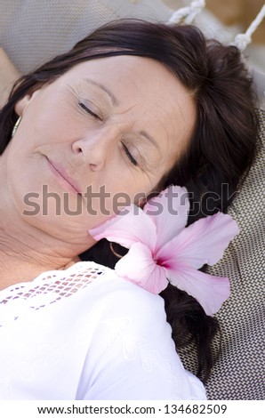 Portrait beautiful mature woman sleeping, with smiling happy and relaxed facial expression, closed eyes and flower in hair.