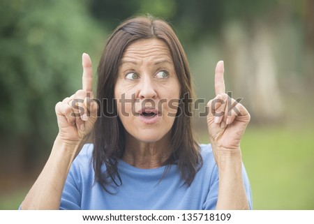 Portrait beautiful mature woman outdoor with great idea, finger up, positive surprised, confident look and facial expression, isolated with blurred background.