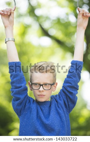 Portrait thoughtful and relaxed young blond teenage boy outdoor with glasses and arms up, with blurred background.