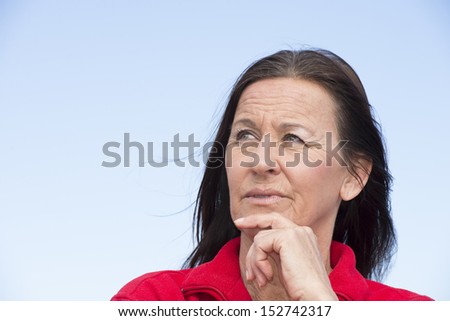 Portrait attractive mature woman with concerned and worried facial expression, fingers on chin, daydreaming and thoughtful, outdoor with sky as background and copy space.