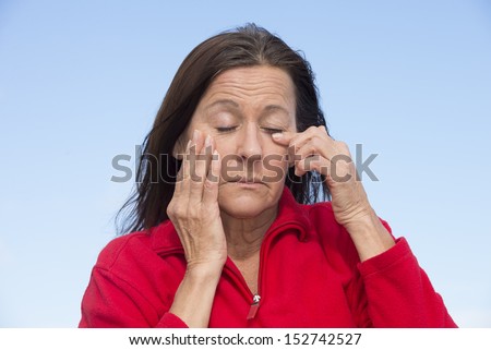 Portrait attractive mature woman with tired, exhausted and stressed facial expression, closed eyes and hands on chin, outdoor with blue sky as background.