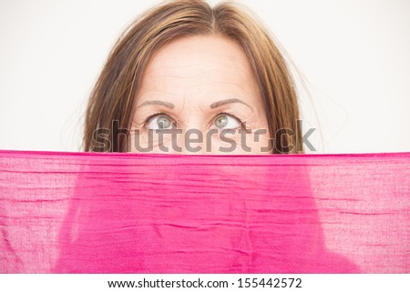 Portrait attractive middle aged woman hiding behind pink cloth, crossed-eyed, funny look, white background.