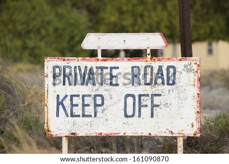 Rusty Warning sign for Limited or restricted access on private road to private property, with blurred background of buildings.