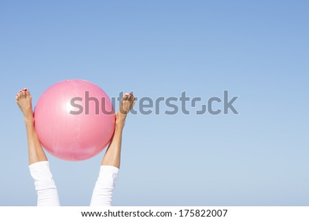 Female legs up in the air with pink exercising ball, isolated on blue sky and copy space.