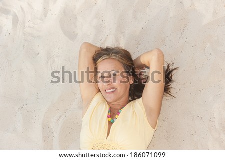 Portrait happy attractive mature woman lying relaxed smiling on sand at beach looking upward into camera, enjoying leisure time, copy space.