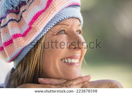 Portrait attractive mature woman with beanie hat to keep warm in winter, friendly relaxed smiling, blurred background outdoor and copy space.