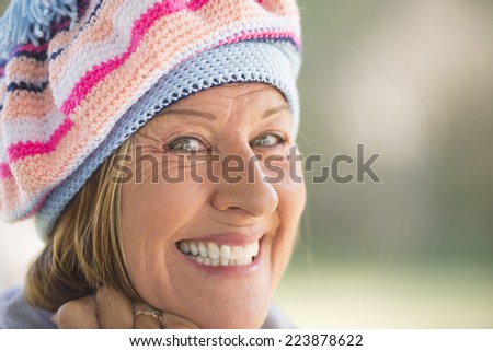 Portrait attractive mature woman with beanie cap to keep warm in winter, friendly confident smiling, blurred background outdoor and copy space.