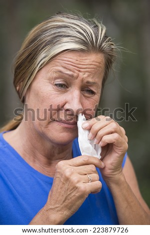 Portrait attractive mature woman with tissue stuffed in running nose, suffering  from cold, flu or hay fever allergy, outdoor blurred background.