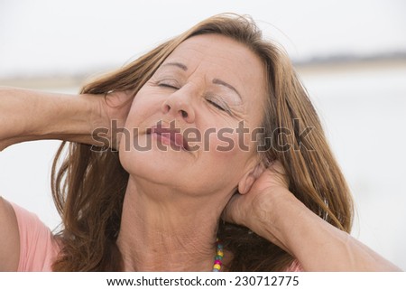 Portrait attractive mature woman posing happy smiling with hands behind head and closed eyes, relaxed meditating, bright outdoor background and copy space.