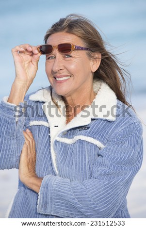 Portrait of attractive mature woman posing happy confident and relaxed smiling  outdoor in warm jacket and sunglasses in cold winter, blurred background.