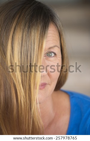 Portrait attractive woman with brunette hair covering half face, one eye confident mysterious upward look, blurred background.