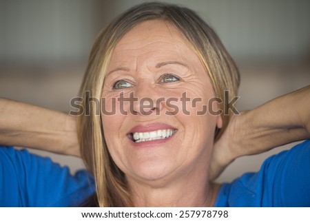 Portrait attractive mature woman with joyful happy confident facial expression, smiling, hands behind neck, blurred background.