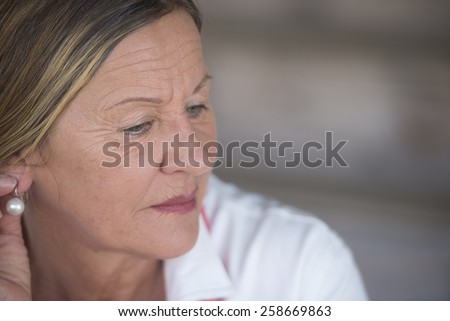 Portrait elegant attractive mature woman with sad lonely concerned depressed expression, blurred background, copy space.