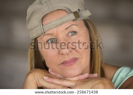 Portrait attractive fit active mature woman wearing green sporty top and cap, thoughtful relaxed, chin resting on hands, blurred background, copy space.