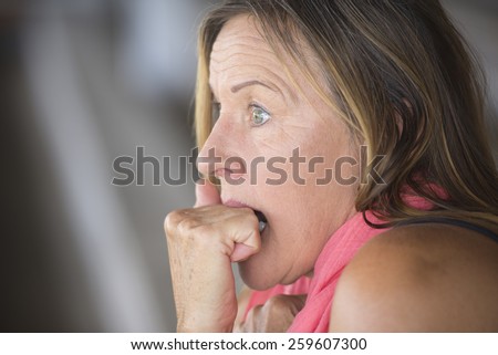 Portrait scared mature woman, fearful, shocked stressed, worried facial expression, nail biting, hand between teeth, blurred background, copy space.