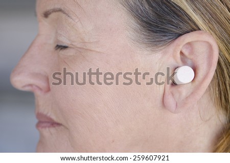 Profile Portrait attractive senior woman blocking sound with ear plug and closed eyes.