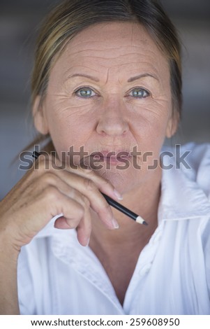 Portrait confident creative attractive mature business woman, thoughtful, serious, with pen in hand, blurred background.