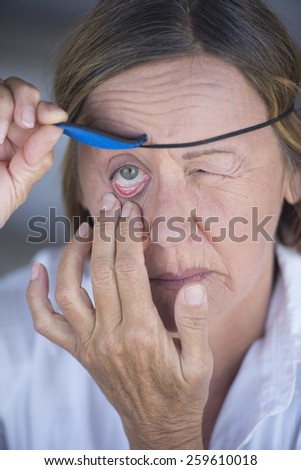 Portrait frustrated attractive mature woman lifting eye patch worn as protection after injury, blurred background.