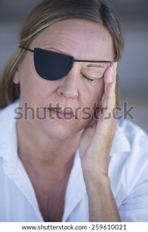 Portrait tired attractive mature woman wearing eye patch as protection after injury, closed eyes, blurred background.