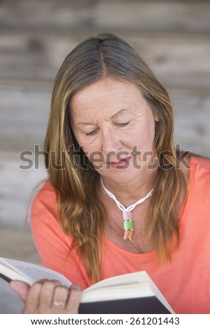 Portrait attractive mature woman reading a book for relaxing entertainment, inspiration, blurred background.