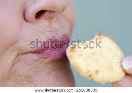 Close up image of mature woman enjoying eating cookie as sweet snack.