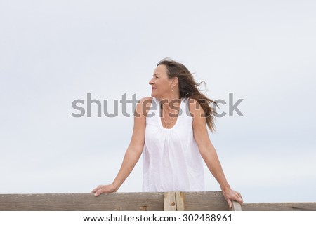 Portrait of confident attractive senior woman posing friendly smiling outdoors, wearing white blouse, bright sky as background and copy space.