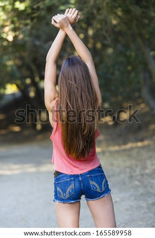 Young brunette with pink shirt and jeans shorts posing with her arms up