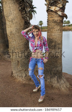Young teen girl in pink flannel shirt posing in front of two palm trees