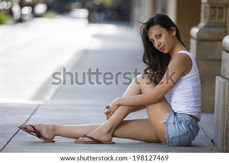 Young hispanic lady sitting on the sidewalk