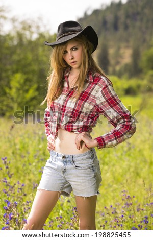 Beautiful girl in denim shorts and red flannel shirt posing with a cowboy hat
