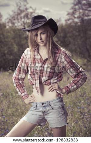 Beautiful cowgirl model wearing cowboy hat and wearing  tied up flannel shirt