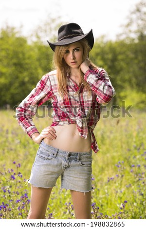Beautiful and young woman posing in red flannel shirt and wearing cowboy hat