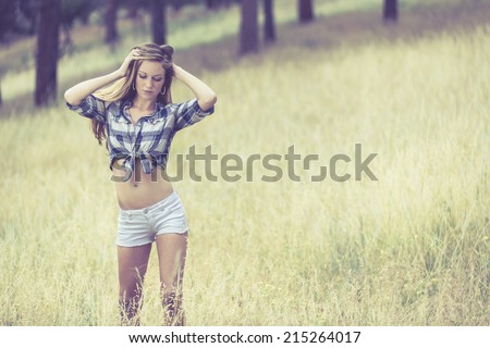 Woman in tight white jeans shorts and tied up blue flannel shirt posing with both hands up